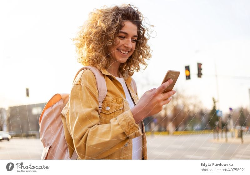 Beautiful young woman with curly hair smiling and using smartphone natural sunlight urban city hipster stylish positive sunny cool afro joy healthy freedom