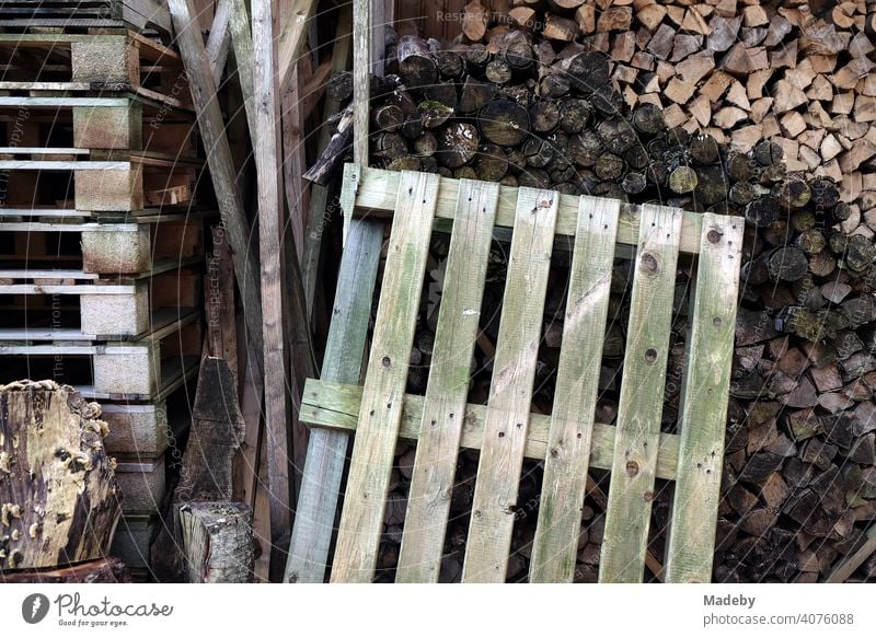 Old wooden pallets and stacked logs for the fireplace in front of a house in Oerlinghausen near Bielefeld on the Hermannsweg in the Teutoburg Forest in East Westphalia-Lippe
