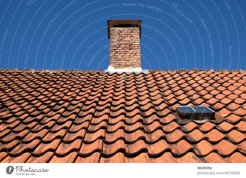 Red-brown curved roof tiles on the roof of an old building with chimney in the sunshine in Oerlinghausen near Bielefeld on the Hermannsweg in the Teutoburg Forest in East Westphalia-Lippe