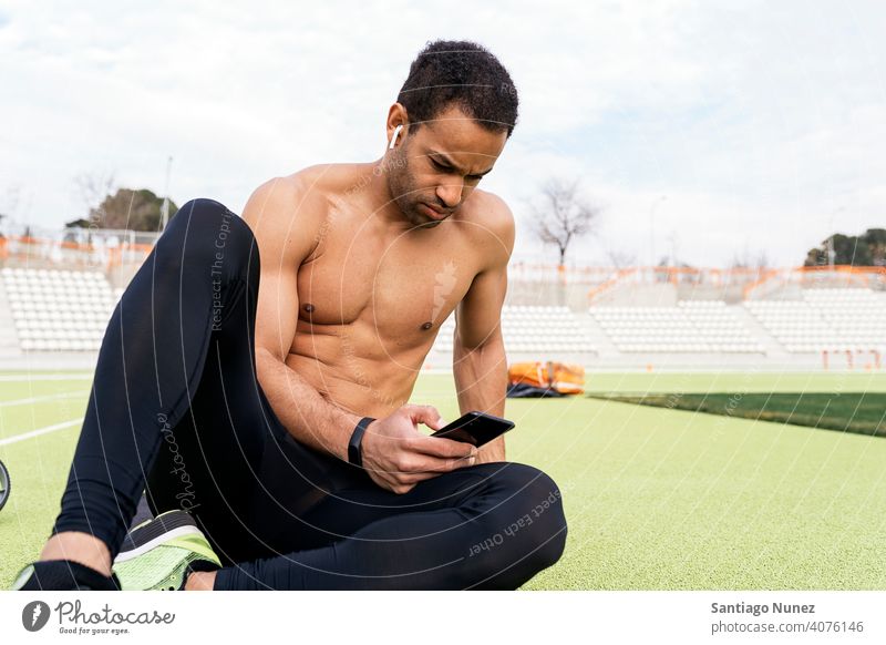 Front view of an Athlete Using Phone in Athletic Track sports track using phone sitting black man rest resting floor background bleachers runner sports wear