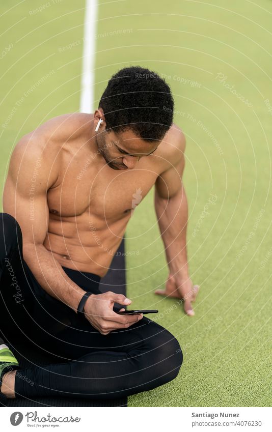 Side view of an Athlete Using Phone in Athletic Track sports track using phone sitting black man rest resting floor background bleachers runner sports wear