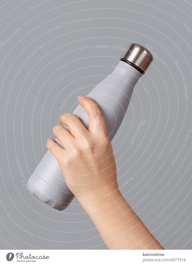 Hand with grey reusable insulated bottle on grey background hand mockup ecologic water steel thermo aluminum blank close up concept copy space negative space