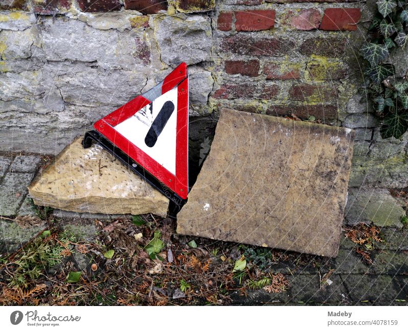 Old broken warning triangle on big stones at the roadside on cobblestones in front of brickwork in autumn in the old town of Oerlinghausen near Bielefeld in the Teutoburg Forest in East Westphalia-Lippe