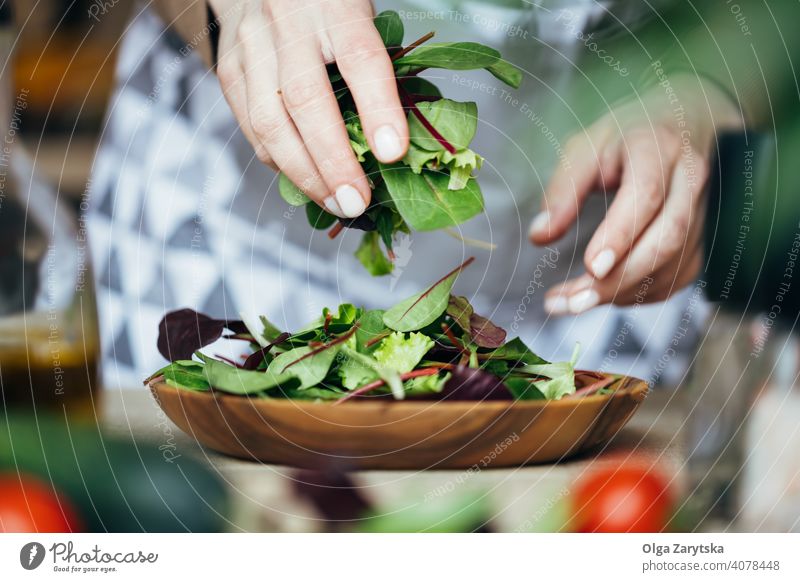 Woman putting a mix of salad on a wooden plate. hand midsection female selective focus close up making tomato arugula red chard vegan food healthy white