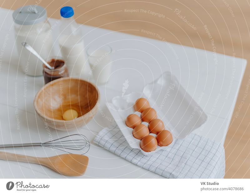 Cooking ingredients on kitchen table. View from above of eggs, milk and flour, whisk and wooden spatula near. Utensils and fresh products beater bowl calcium