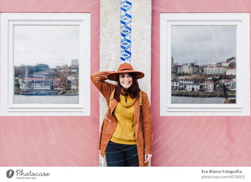 portrait of young beautiful woman standing at porto wall wearing modern hat enjoying views. Travel concept Porto travel windows pink reflection city urban river