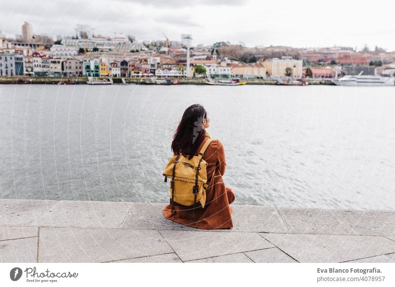 back view of young beautiful woman sitting by the river at sunset enjoying Porto views. Travel concept travel city sightseeing urban caucasian people