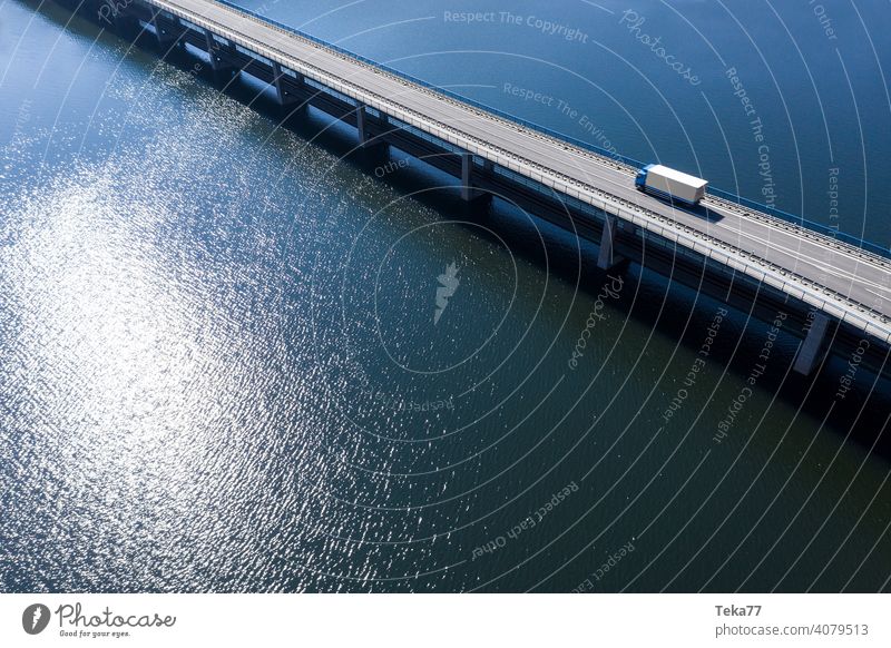 a truck driving on a bridge in the water truck drving future future tansportation sea lake bridge in water from above sun modern transportationmodenr truck