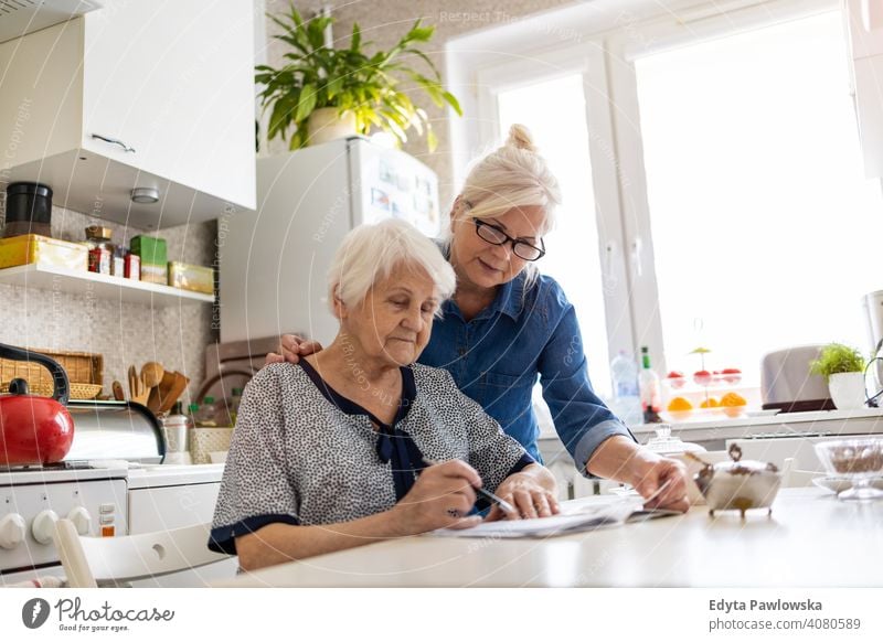 Mature woman helping elderly mother with paperwork will document discussing writing finance money confusion reading kitchen domestic assistance support