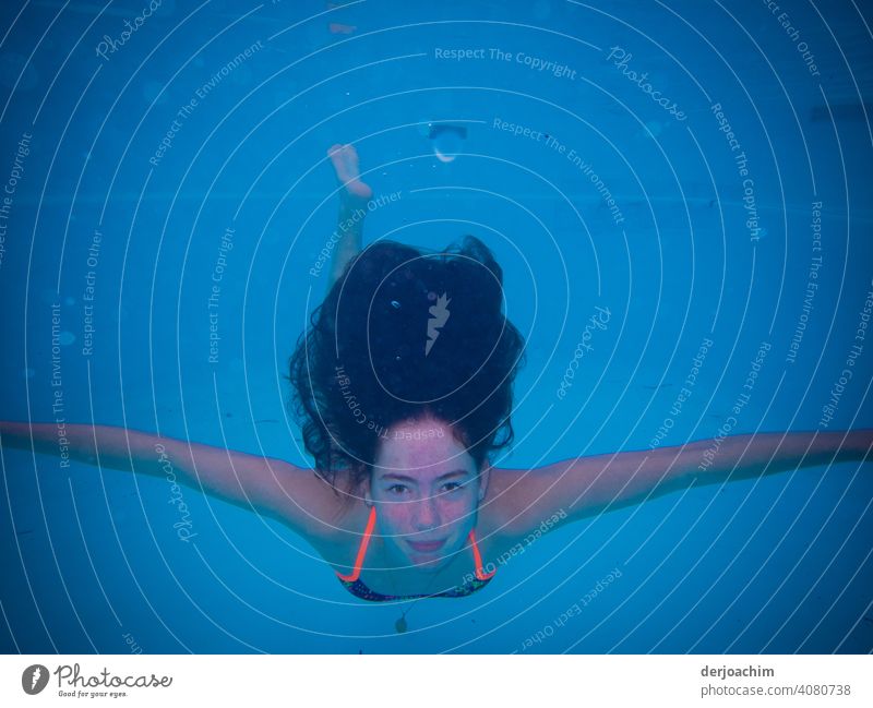 A young girl swims, in blue water, under with her arms spread wide and her dark hair floating above her. Floating Grand piano Water Nature Blue Summer Sun