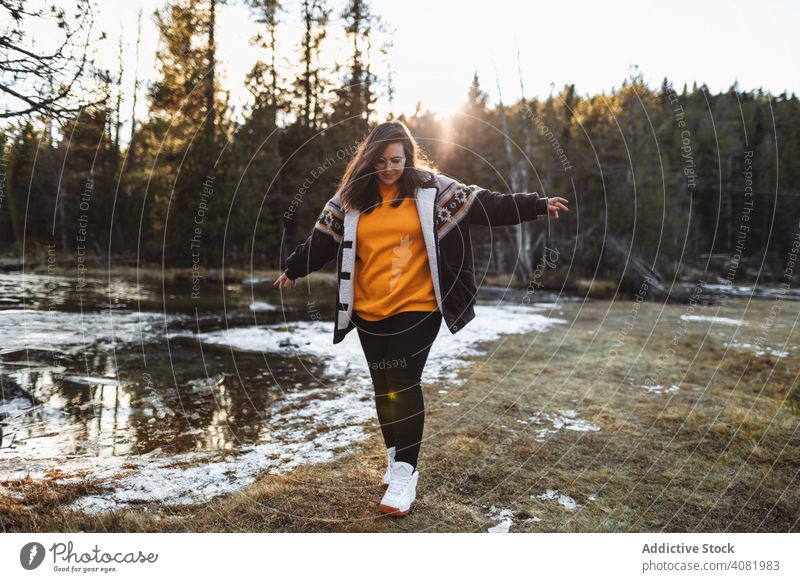 Cheerful young woman on pond in forest happy hiker cheerful traveling joyful tourism meadow snow weather leisure footpath trees sunlight female lifestyle