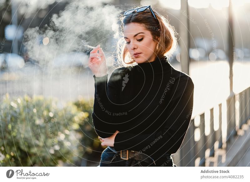Pretty woman smoking on street cigarette exhaling style sunny daytime female city urban young lifestyle leisure fume rest relax lady habit tobacco sensual