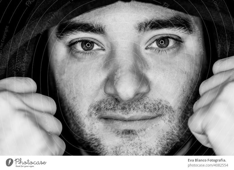 close up portrait of a young man covering with a hood. studio shot. led ring reflection in the eyes head white people male black dramatic person lifestyle