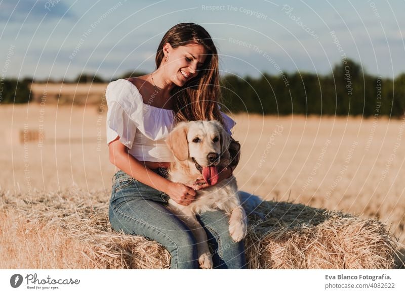 young beautiful woman walking with her golden retriever dog on a yellow field at sunset. Nature and lifestyle outdoors summer fashion harmony beauty romantic