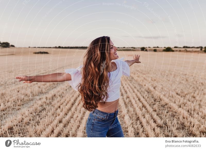 Summer Girl enjoying nature on yellow field. Beautiful young woman dancing Outdoors. Long hair in the wind. Happiness and lifestyle. Back view sunset beauty