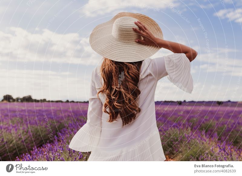 charming Young woman with a hat and white dress in a purple lavender field at sunset. LIfestyle outdoors. Back view meadow beauty joy leisure freedom farm
