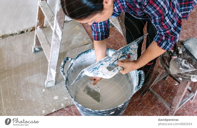 Female builder working picking plaster with spatula unrecognizable woman plasterer picking up mortar gypsum plaster trowel construction reform house bucket
