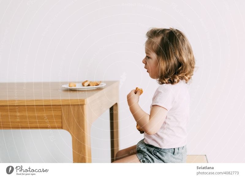 A little girl sits at a table and eats cookies child happy biscuits nutrition food young childhood cute kitchen face people healthy home sweet family kid