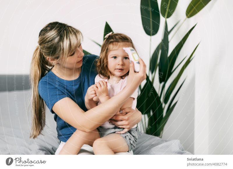 A worried mother checks her daughter's temperature with an electronic thermometer baby holding checking parent sick kid childhood childcare ill home motherhood