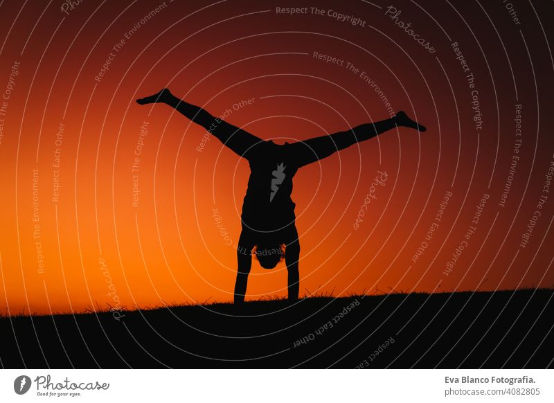 silhouette of young man in a park doing yoga sport. orange sky background. healthy lifestyle. back light concentration position people body meditating