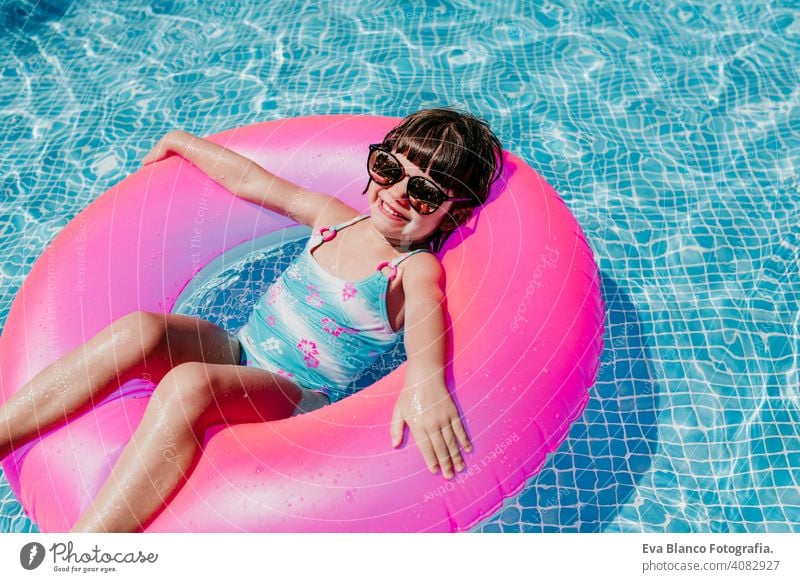 beautiful kid girl floating on pink donuts in a pool. Wearing sunglasses and smiling. Fun and summer lifestyle activity beauty outdoor teenager swimming
