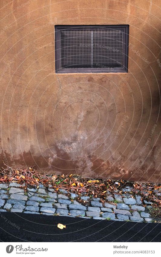Basement window in an old washed out reddish brown facade with autumn leaves and cobblestones in Wettenberg Krofdorf-Gleiberg near Giessen In Hesse Window