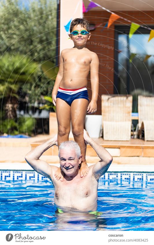 Grandfather carrying his grandson on his shoulders in a swimming pool backyard balance blue boy carefree caucasian child childhood children cooling courtyard