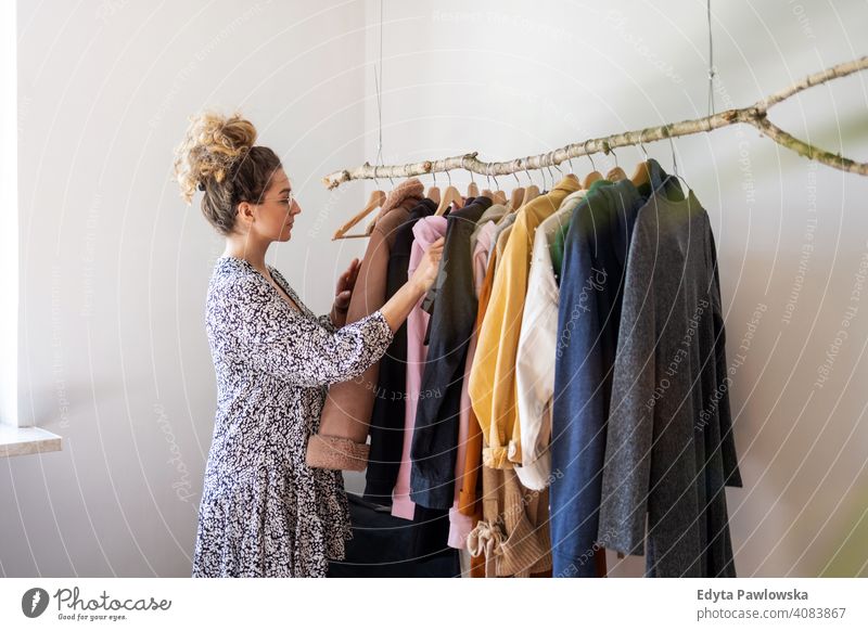 Young woman shopping at a clothing boutique fashion clothes fashionable rack choosing retail store sale hanger customer style shopper shopaholic wardrobe choice