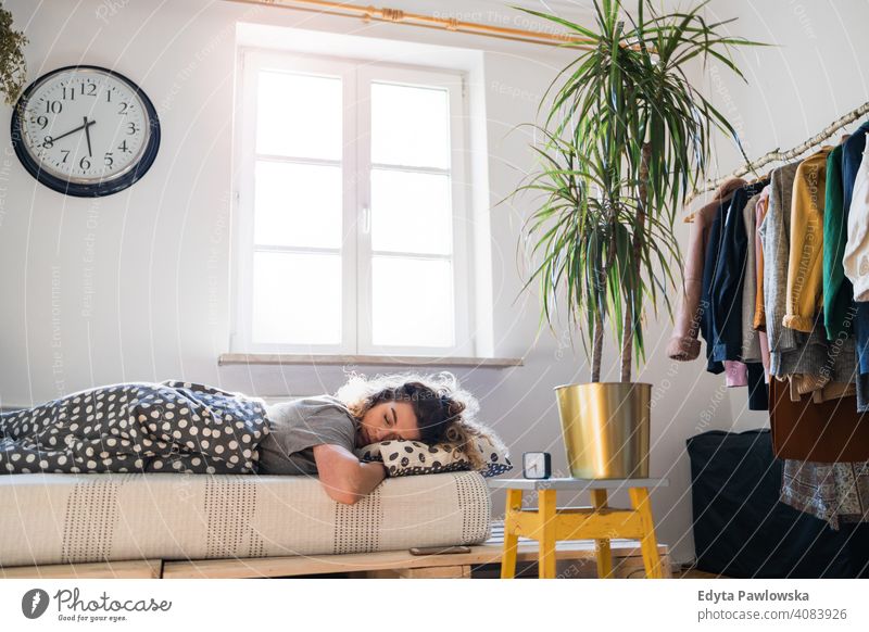 Young woman asleep in bed morning clock resting relaxation sleeping awake alarm clock sleepy waking up apartment leisure bedroom house home alone people