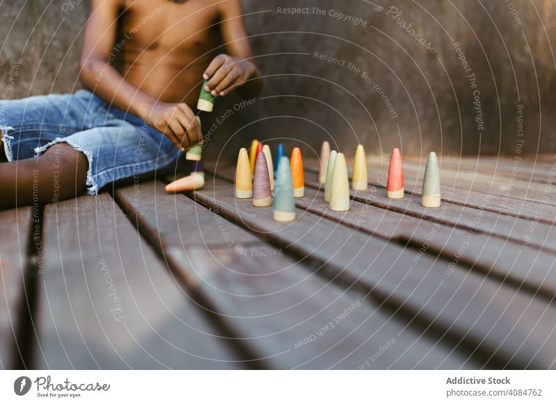 Crop black kid playing with cones boy sitting sunny daytime shirtless game colorful lifestyle leisure rest relax african american ethnic little fun child wooden