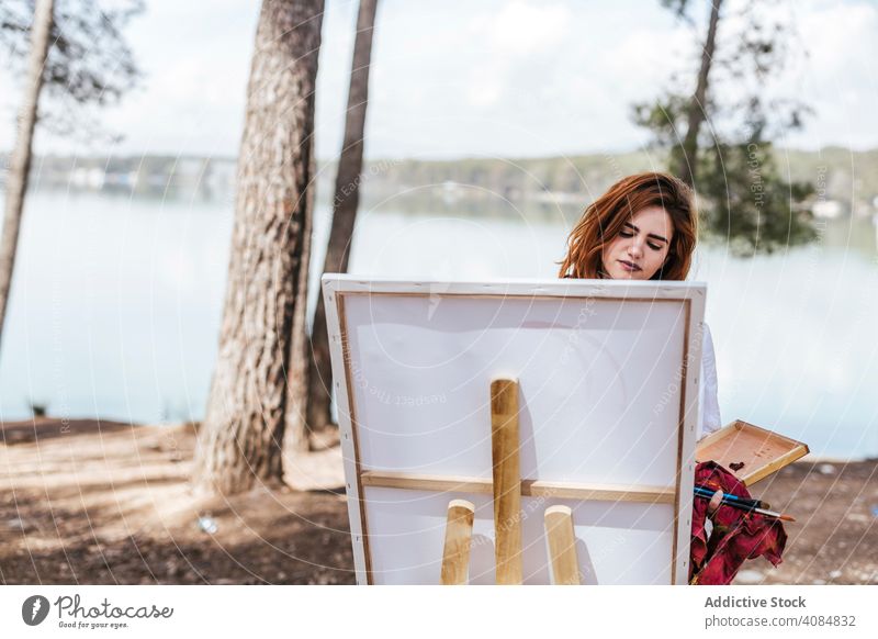 Young woman painting in countryside artist nature lake easel palette landscape summer lifestyle leisure female casual focused concentrated skill talent