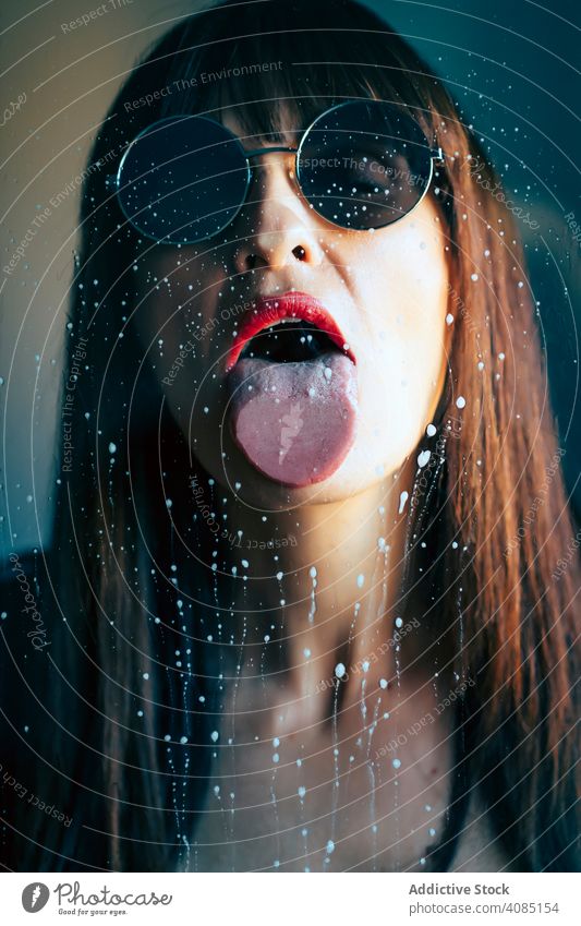 Sexy woman licking wet glass makeup stylish sensual passion adult sexy female transparent glamour lipstick red liquid drops style trendy lady bright dirty