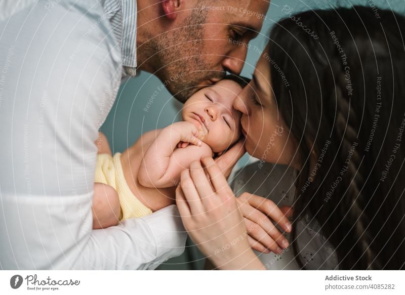 Parents holding baby in room parents couple kiss kissing touching care tender family love home bonding man woman mother father together joy newborn infant kid