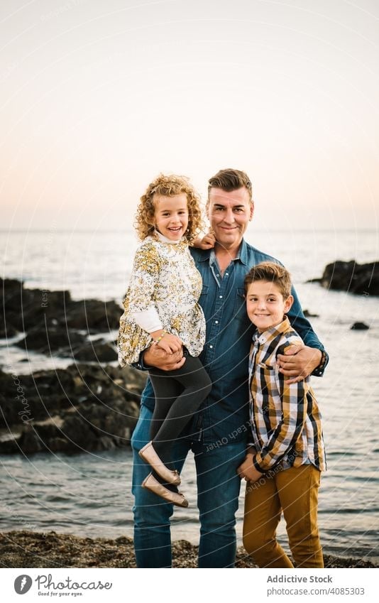 Father with her children at beach family seaside vacation kids smiling hug hugging embrace father man middle-aged daughter son girl togetherness summer sand