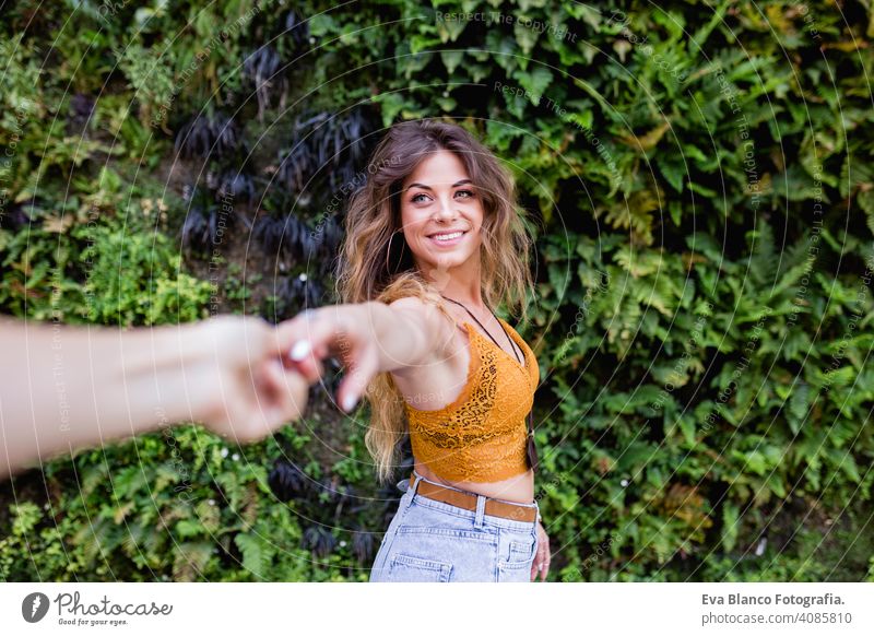 portrait of a young blonde beautiful woman at the street smiling. Holding hands in a follow me pose. Green vegetation background. Lifestyle outdoors. Summertime