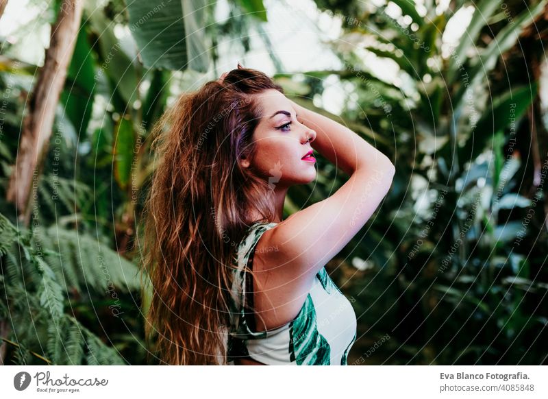 portrait of beautiful blonde young woman smiling at sunset in a green house surrounded by tropical plants. Happiness and lifestyle concept caucasian toothy cute