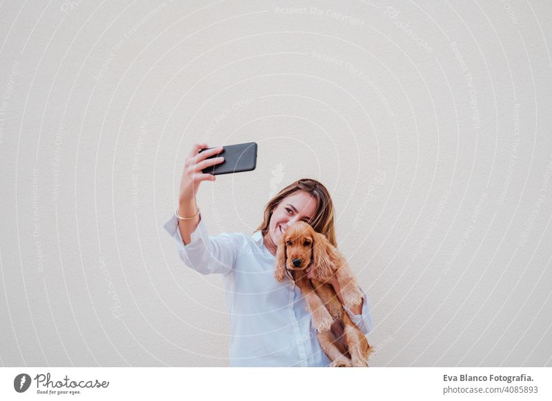 young woman at the street with her cocker dog taking a picture with mobile phone. Lifestyle outdoors with pets technology selfie friendship city beautiful