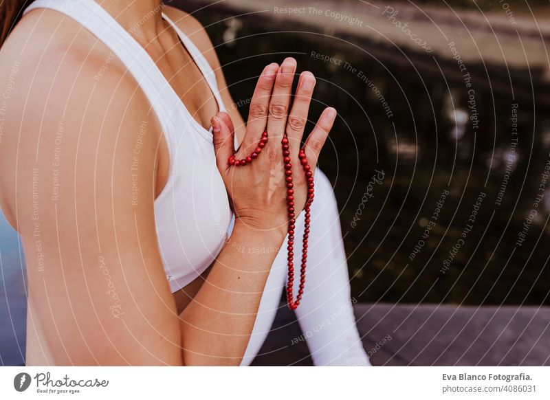 close up view of unrecognizable young asian woman doing yoga in a park. Sitting on the bridge with praying hands position and using Mala necklace. Yoga and healthy lifestyle concept