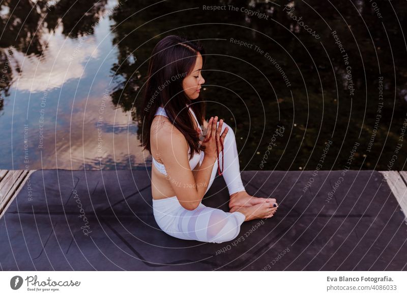 young beautiful asian woman doing yoga in a park. Sitting on the bridge with reflection on the water lake. Yoga and healthy lifestyle concept practicing balance