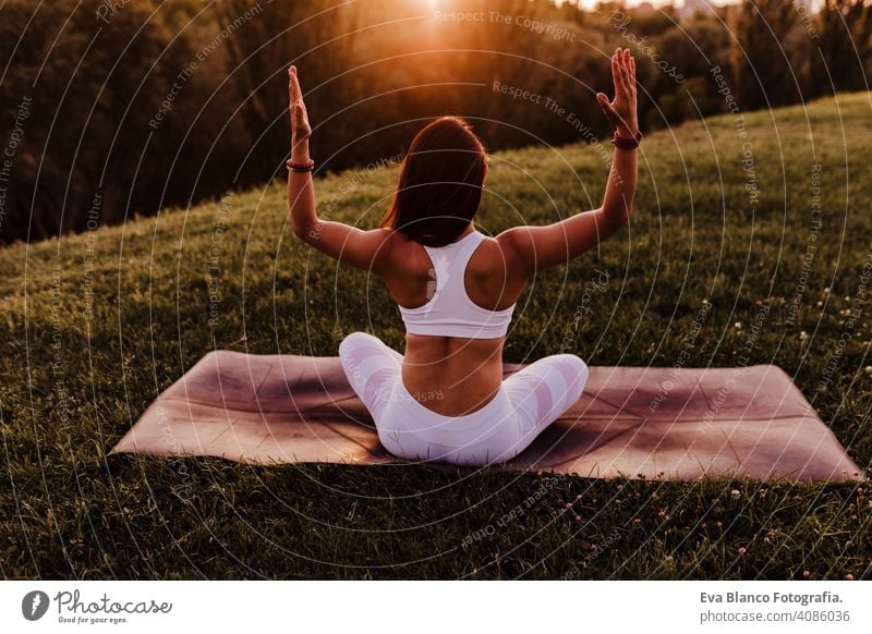 young beautiful asian woman doing yoga in a park at sunset. Yoga and healthy lifestyle concept. Back view summer happy enjoyment sport sportive relax relaxation