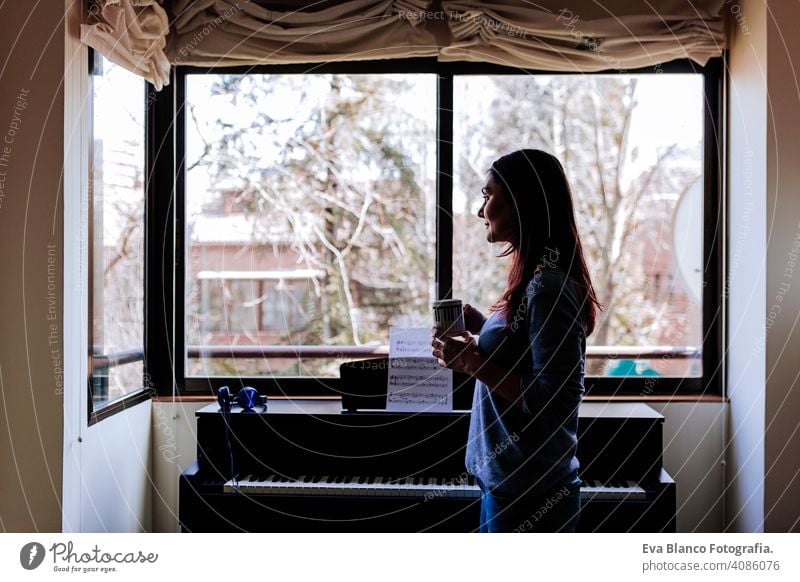 young woman holding a cup of coffee and ready to play piano by reading a music sheet. Music concept indoors style human key note lesson caucasian press chord