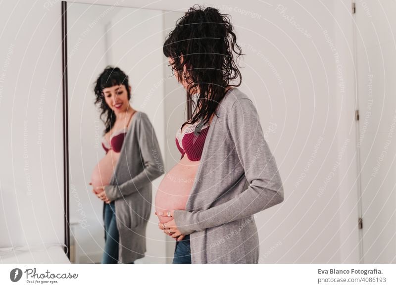 portrait of young pregnant woman at home looking into the mirror lifestyle expecting window daytime expectation beauty parenting maternal expectant baby indoor