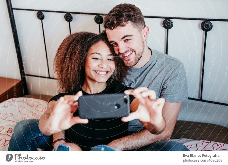 happy couple in love at home. Afro american woman and caucasian man taking a selfie with mobile phone. ethnic love concept afro american bed indoors valentine