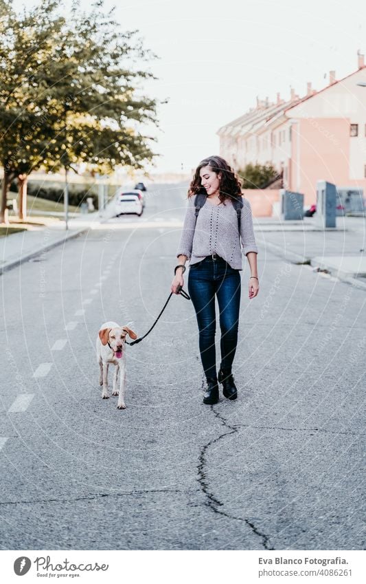 young woman and her dog outdoors walking by the street. autumn season park love pet owner sunny beautiful happy smile mixed race purebred breed hug backpack