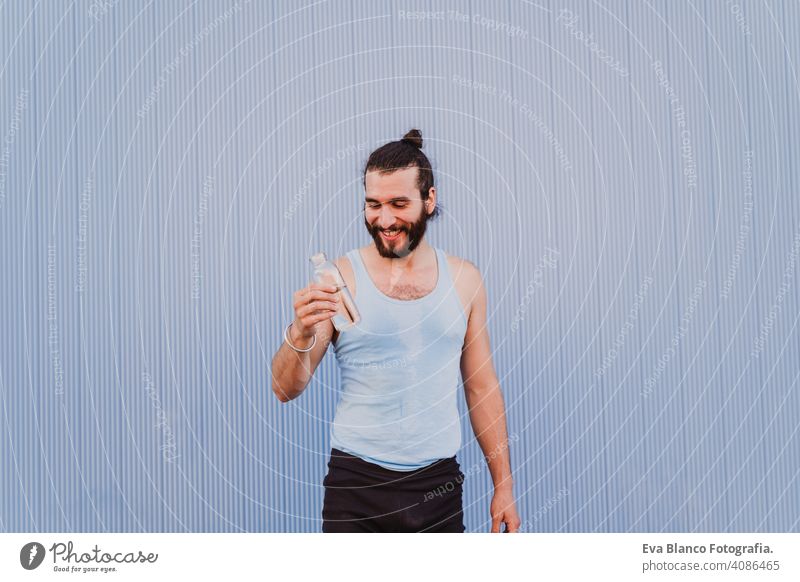 man in the city practicing yoga sport and drinking water. blue background. healthy lifestyle outdoors muscular young handsome hispanic caucasian sportswear