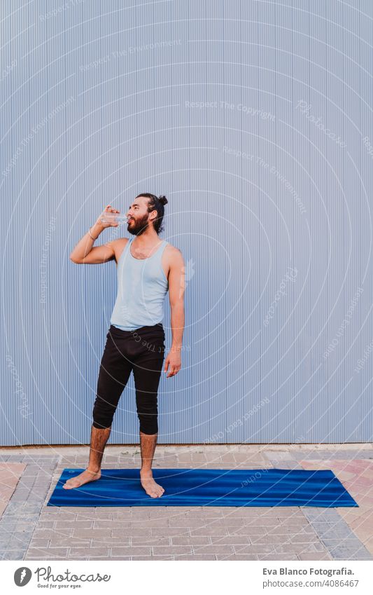 man in the city practicing yoga sport and drinking water. blue background. healthy lifestyle outdoors muscular young handsome hispanic caucasian sportswear