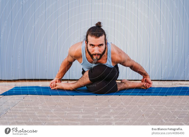 man in the city practicing yoga sport. blue background. healthy lifestyle outdoors muscular young handsome hispanic caucasian sportswear urban concentration