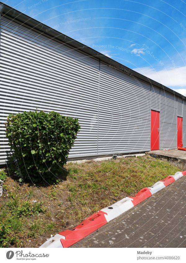 Green shrub in front of a modern aircraft hangar with a facade of corrugated iron with red doors at the glider airfield in Oerlinghausen near Bielefeld on the Hermannsweg in the Teutoburg Forest in East Westphalia-Lippe