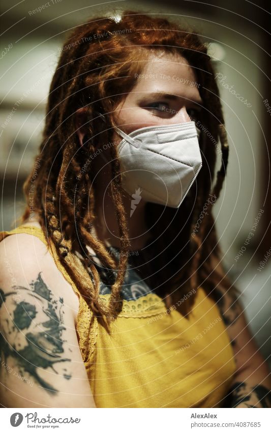 Young woman with dreadlocks and mask looks into the camera Woman Dreadlocks Mask covid19 Protection Top Yellow pretty fit Concealed inside safeguarded Skin