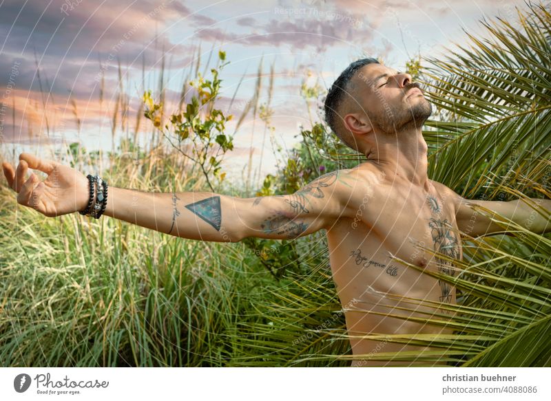 man spreads his arms and breathes in nature Man portrait 30 years Naked Nature plants palms Garden Happy in harmony Sky Joy Climate Climate protection Breathe